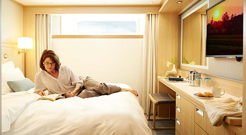 A woman lounging on a Viking Standard Stateroom bed, reading a book.