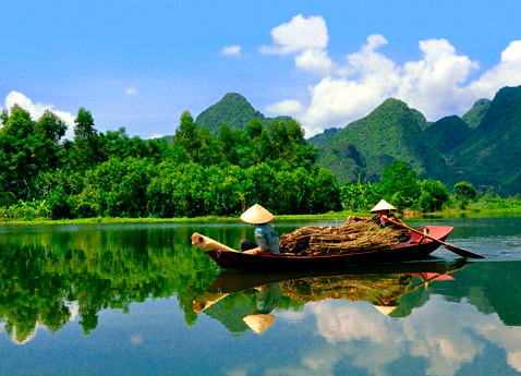 Two boatmen navigate the Mekong River with green mountains and a bright blue sky.