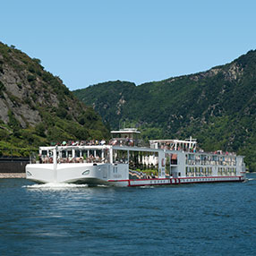 Photo of a ship cruising a river line with green hills in the background